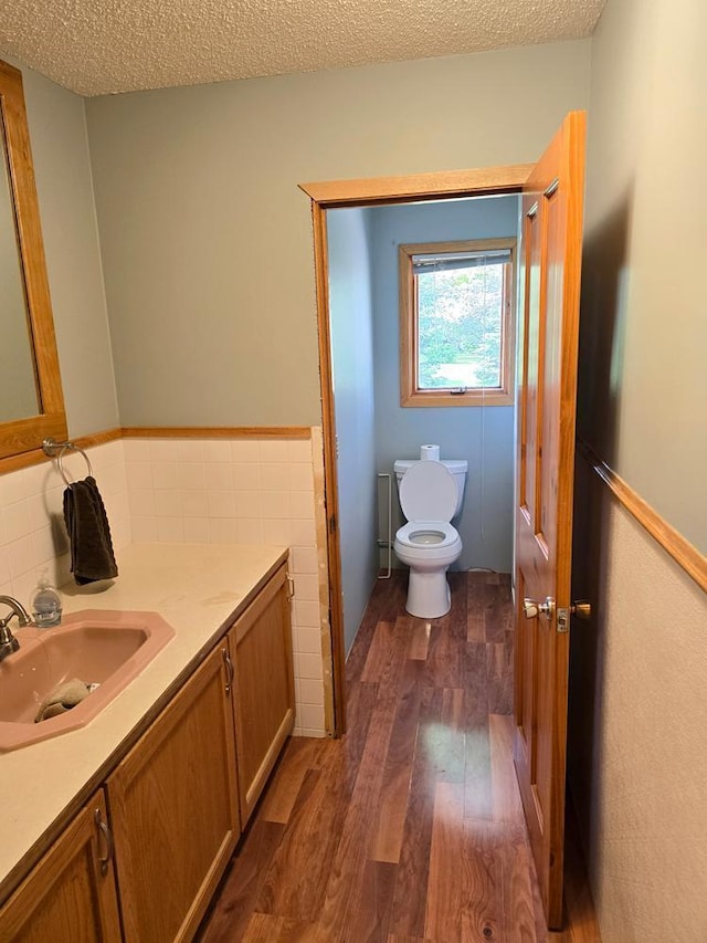 bathroom with wood-type flooring, a textured ceiling, toilet, vanity, and tile walls