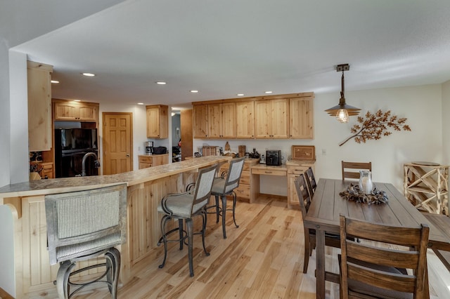 kitchen with black fridge, hanging light fixtures, light hardwood / wood-style floors, kitchen peninsula, and a breakfast bar area