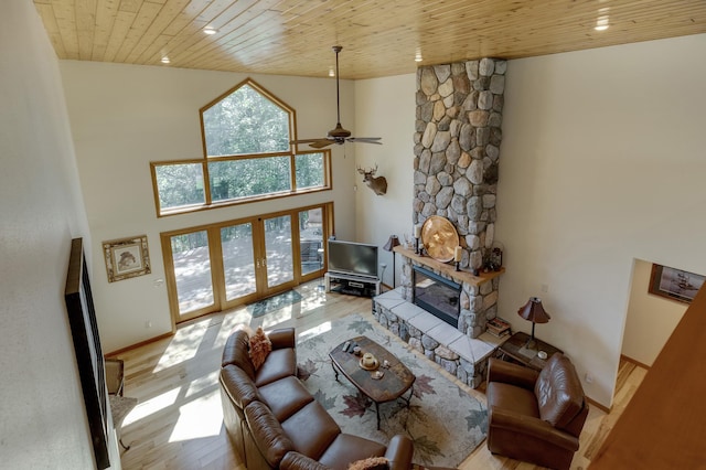 living room with a high ceiling, a stone fireplace, ceiling fan, light wood-type flooring, and wood ceiling