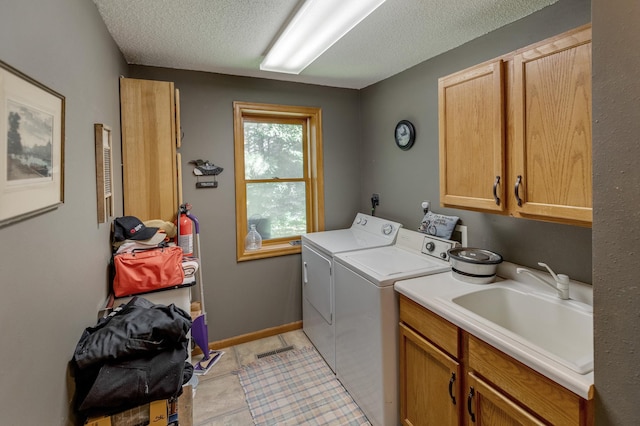 laundry room featuring cabinets, a textured ceiling, washing machine and dryer, and sink