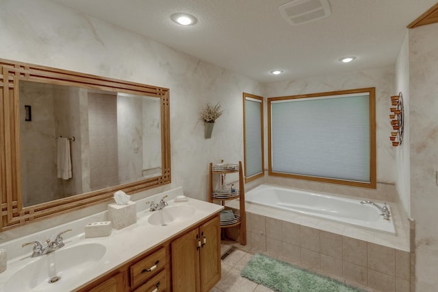 bathroom with a textured ceiling, vanity, a relaxing tiled tub, and tile patterned floors