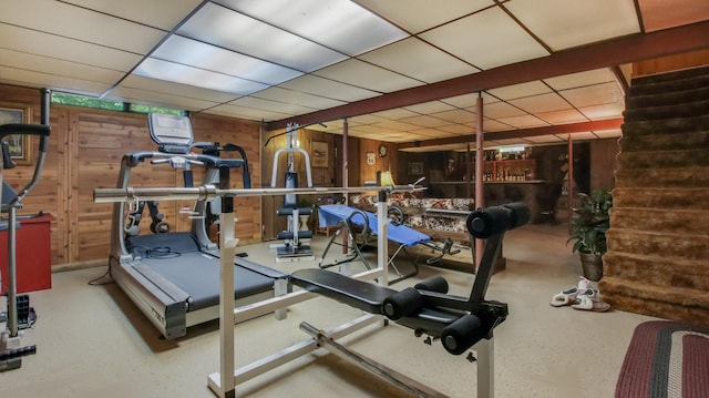 exercise room with a drop ceiling and wood walls