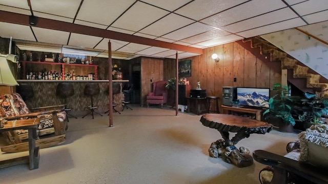 basement with a paneled ceiling, bar, and wood walls