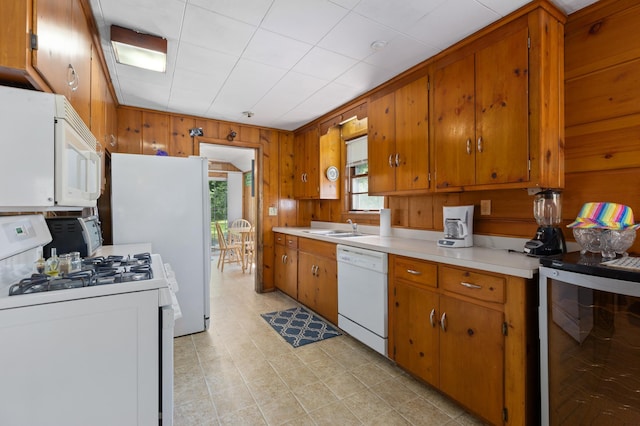 kitchen featuring wine cooler, white appliances, light tile flooring, wooden walls, and sink