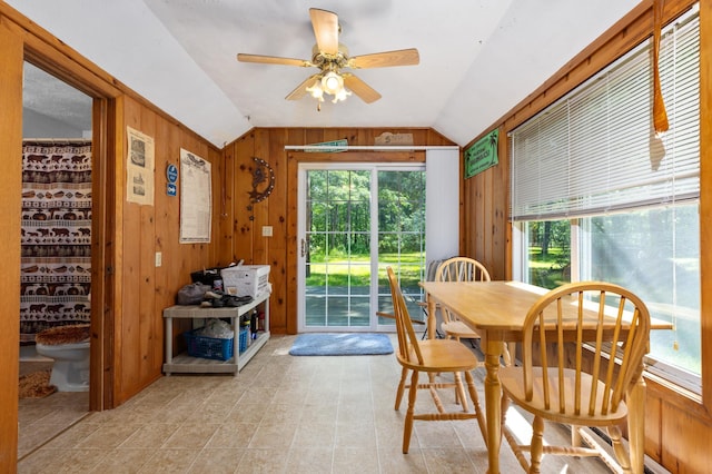 tiled dining room featuring wooden walls, ceiling fan, and vaulted ceiling