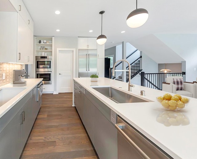 kitchen with stainless steel appliances, decorative light fixtures, dark wood-type flooring, sink, and white cabinets