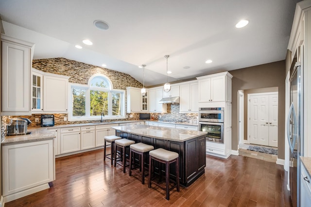 kitchen with a kitchen island, pendant lighting, stainless steel double oven, lofted ceiling, and dark hardwood / wood-style floors