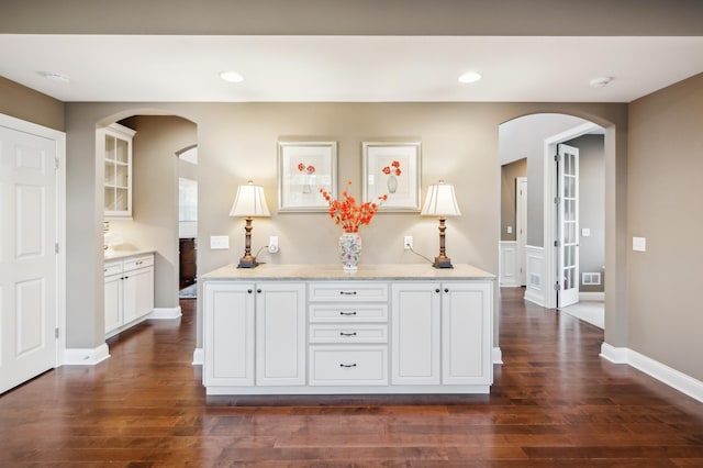 kitchen with light stone counters, white cabinets, and dark hardwood / wood-style flooring