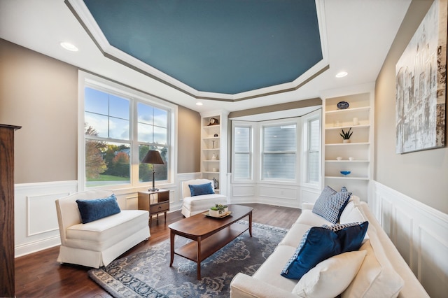 living room with built in shelves, a tray ceiling, crown molding, and dark wood-type flooring