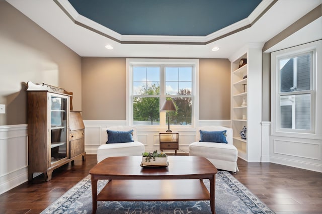 living room with a raised ceiling, built in shelves, ornamental molding, and dark hardwood / wood-style floors