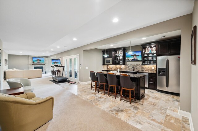 interior space with a kitchen island with sink, a kitchen bar, a fireplace, stainless steel appliances, and backsplash