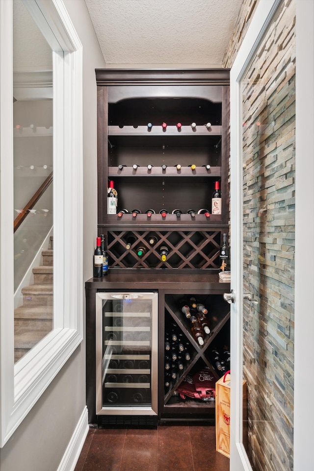 wine area with wine cooler, dark tile patterned flooring, crown molding, and a textured ceiling