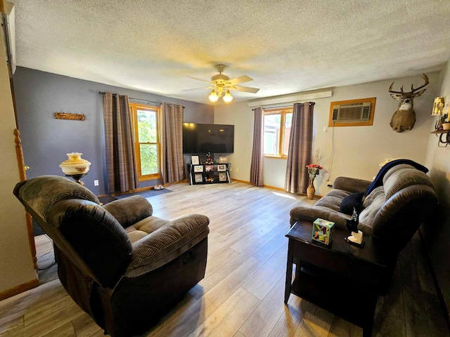 living room featuring a textured ceiling, light hardwood / wood-style flooring, ceiling fan, and an AC wall unit