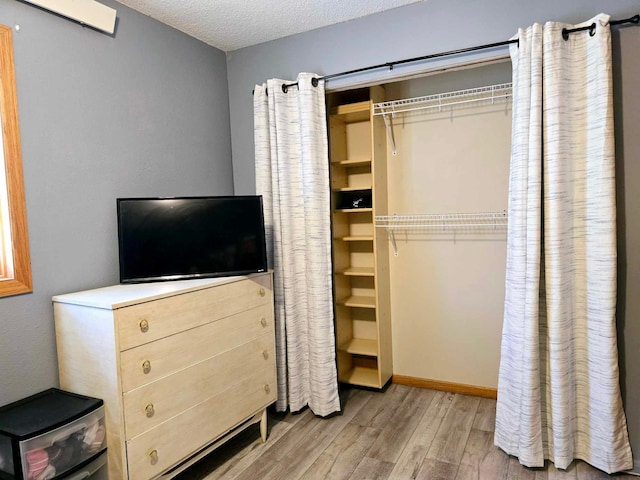 bedroom featuring an AC wall unit, a closet, light hardwood / wood-style floors, and a textured ceiling