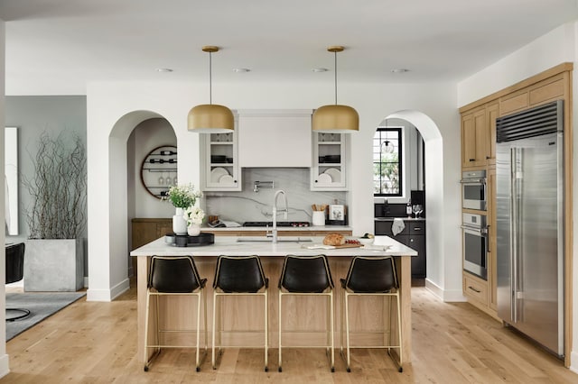 kitchen featuring pendant lighting, a center island with sink, white cabinetry, and built in fridge