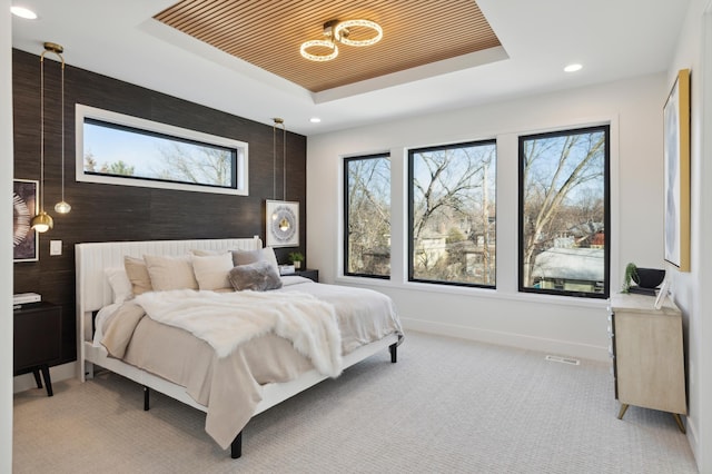 carpeted bedroom with a tray ceiling and multiple windows