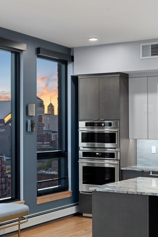 1240 2nd St Unit 1201, Minneapolis, MN 55415 - kitchen with a baseboard heating unit, light wood-type flooring, light stone countertops, backsplash, and stainless steel double oven
