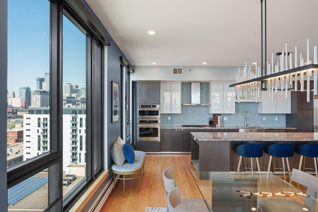 1240 2nd St Unit 1201, Minneapolis, MN 55415 - kitchen featuring wall chimney exhaust hood, a breakfast bar area, gas stovetop, tasteful backsplash, and light wood finished floors