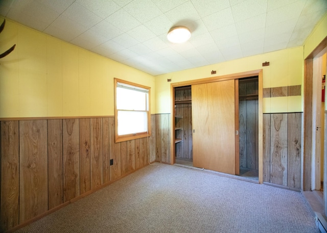 unfurnished bedroom featuring light carpet, a closet, and wood walls