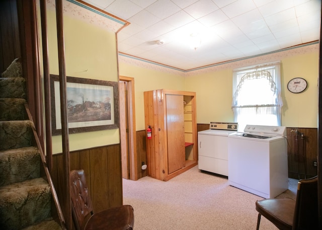 washroom featuring wood walls, crown molding, light carpet, and washing machine and clothes dryer