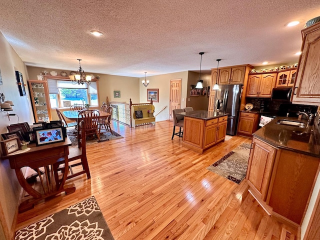 kitchen with a textured ceiling, a center island, stainless steel fridge with ice dispenser, sink, and light hardwood / wood-style flooring