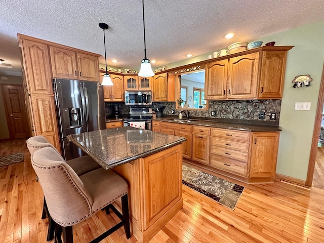 kitchen featuring a textured ceiling, a center island, hanging light fixtures, light hardwood / wood-style flooring, and appliances with stainless steel finishes