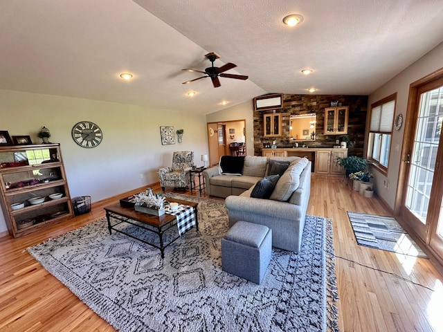 living room with light wood-type flooring, a healthy amount of sunlight, vaulted ceiling, and ceiling fan