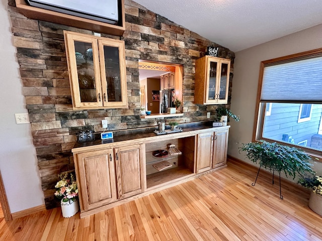 bar with a textured ceiling, light hardwood / wood-style flooring, stainless steel fridge, and vaulted ceiling