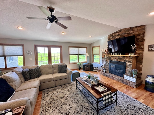 living room with ceiling fan, lofted ceiling, a textured ceiling, hardwood / wood-style flooring, and a fireplace