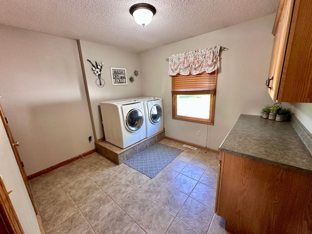 laundry room with cabinets, a textured ceiling, light tile patterned floors, and washing machine and dryer