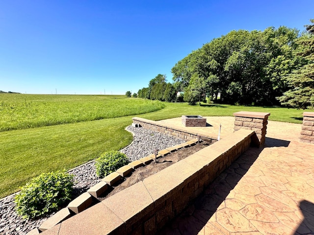 view of community featuring a lawn, a fire pit, a rural view, and a patio area