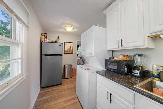 kitchen with dark stone countertops, a textured ceiling, white cabinets, light wood-type flooring, and stainless steel refrigerator