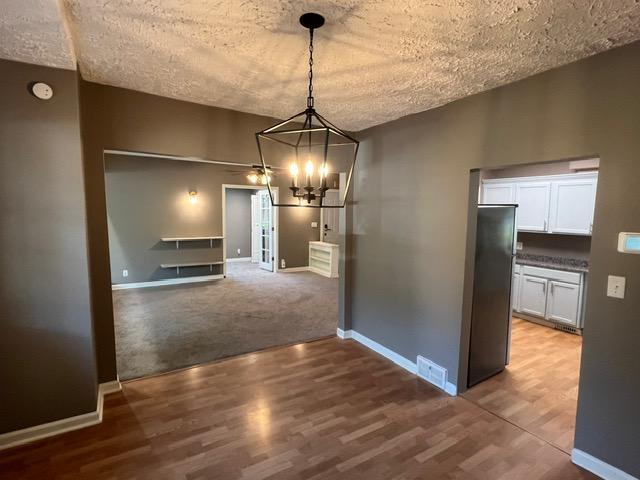 unfurnished dining area with a textured ceiling, carpet, and an inviting chandelier