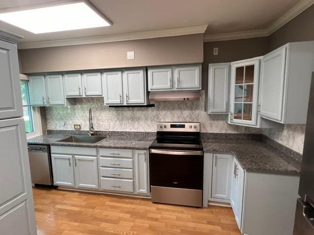 kitchen with appliances with stainless steel finishes, sink, crown molding, and light hardwood / wood-style floors