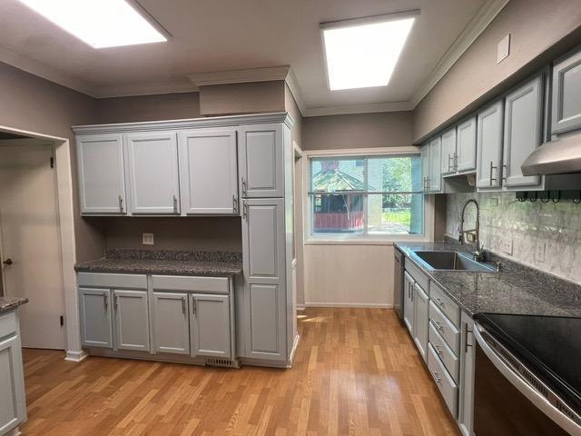 kitchen with gray cabinets, light hardwood / wood-style floors, backsplash, ornamental molding, and sink