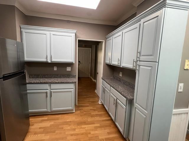 kitchen with light hardwood / wood-style flooring, ornamental molding, and stainless steel fridge