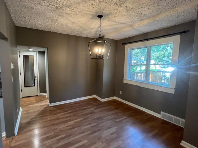 unfurnished dining area featuring wood-type flooring, a textured ceiling, and an inviting chandelier