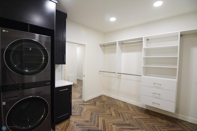 laundry room with stacked washer / drying machine, dark parquet flooring, and cabinets