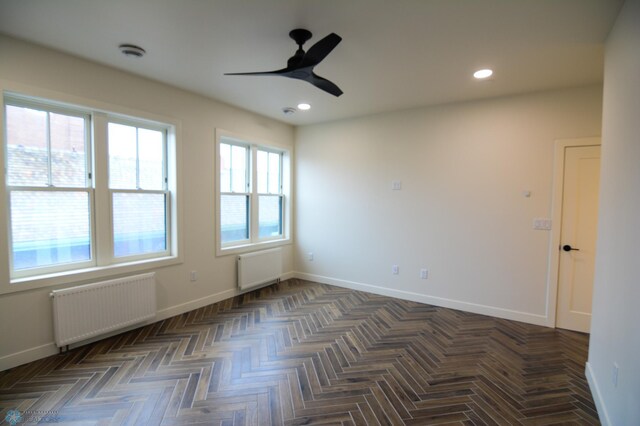 empty room featuring ceiling fan, dark parquet floors, and radiator