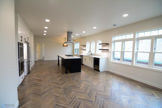 kitchen featuring white cabinetry, island exhaust hood, a kitchen island, black stovetop, and beverage cooler