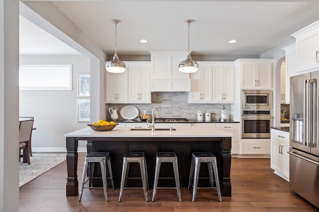 kitchen with a kitchen island with sink, dark hardwood / wood-style flooring, stainless steel appliances, and decorative light fixtures