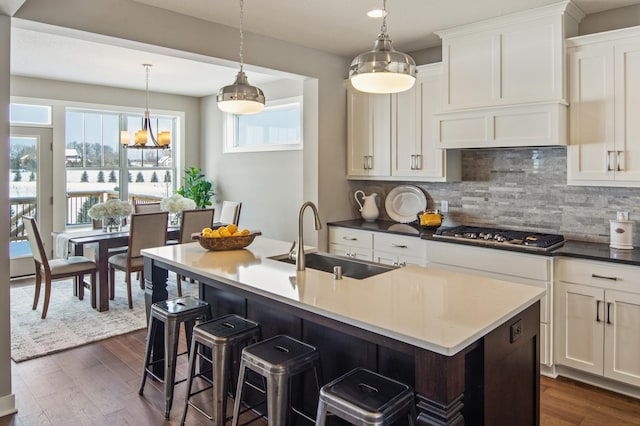 kitchen with tasteful backsplash, stainless steel gas stovetop, a center island with sink, dark wood-type flooring, and sink