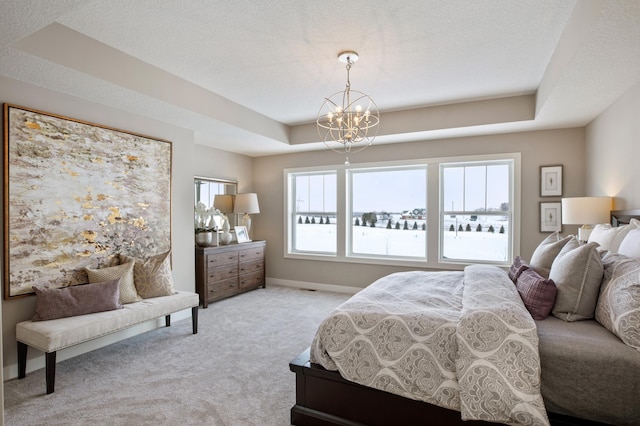 carpeted bedroom with a textured ceiling, a chandelier, and a tray ceiling