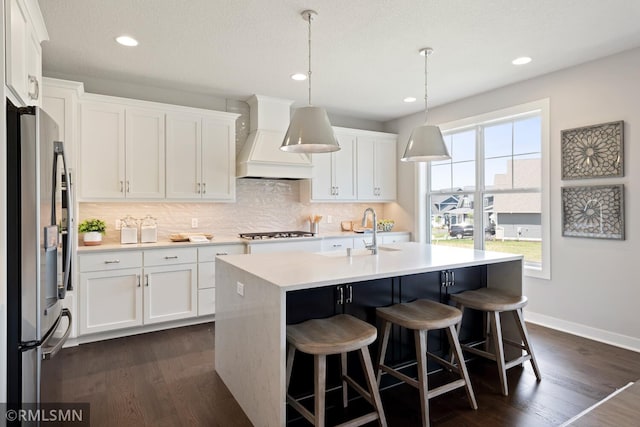 kitchen featuring an island with sink, stainless steel fridge, dark wood-type flooring, sink, and premium range hood