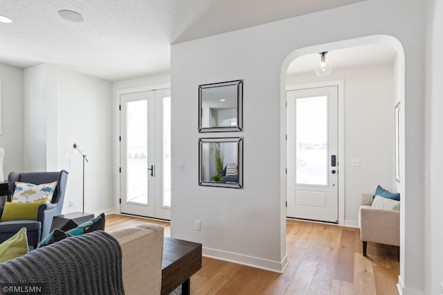 entryway with french doors, light wood-type flooring, and a textured ceiling