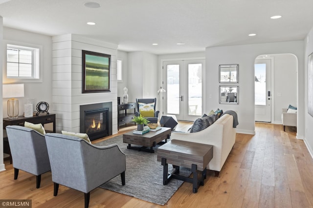 living room with a large fireplace, french doors, and light hardwood / wood-style flooring