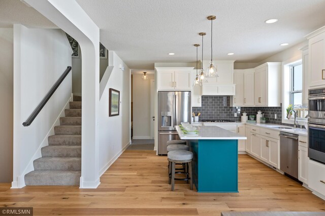 kitchen with white cabinets, sink, light wood-type flooring, appliances with stainless steel finishes, and a kitchen island