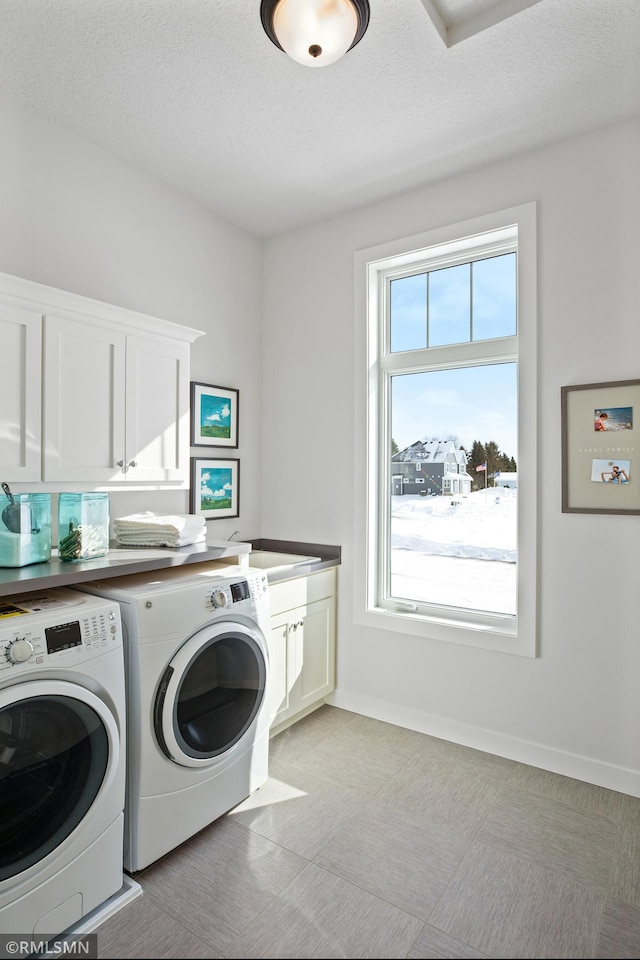 clothes washing area featuring washer and clothes dryer, a healthy amount of sunlight, cabinets, and a textured ceiling