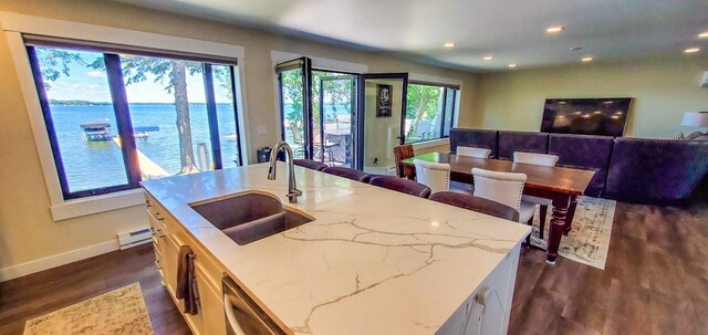 kitchen with dark wood-style floors, baseboards, light stone countertops, a sink, and a water view