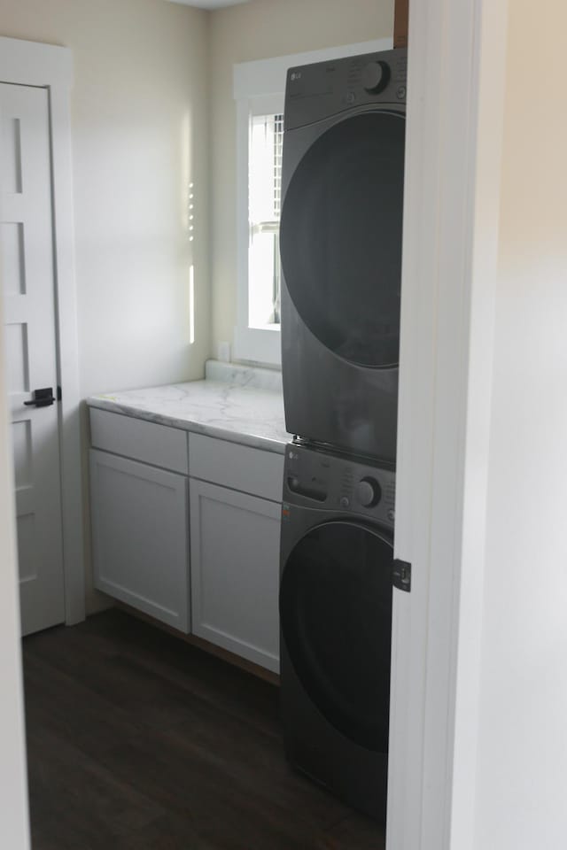 laundry area with dark wood finished floors, cabinet space, and stacked washing maching and dryer